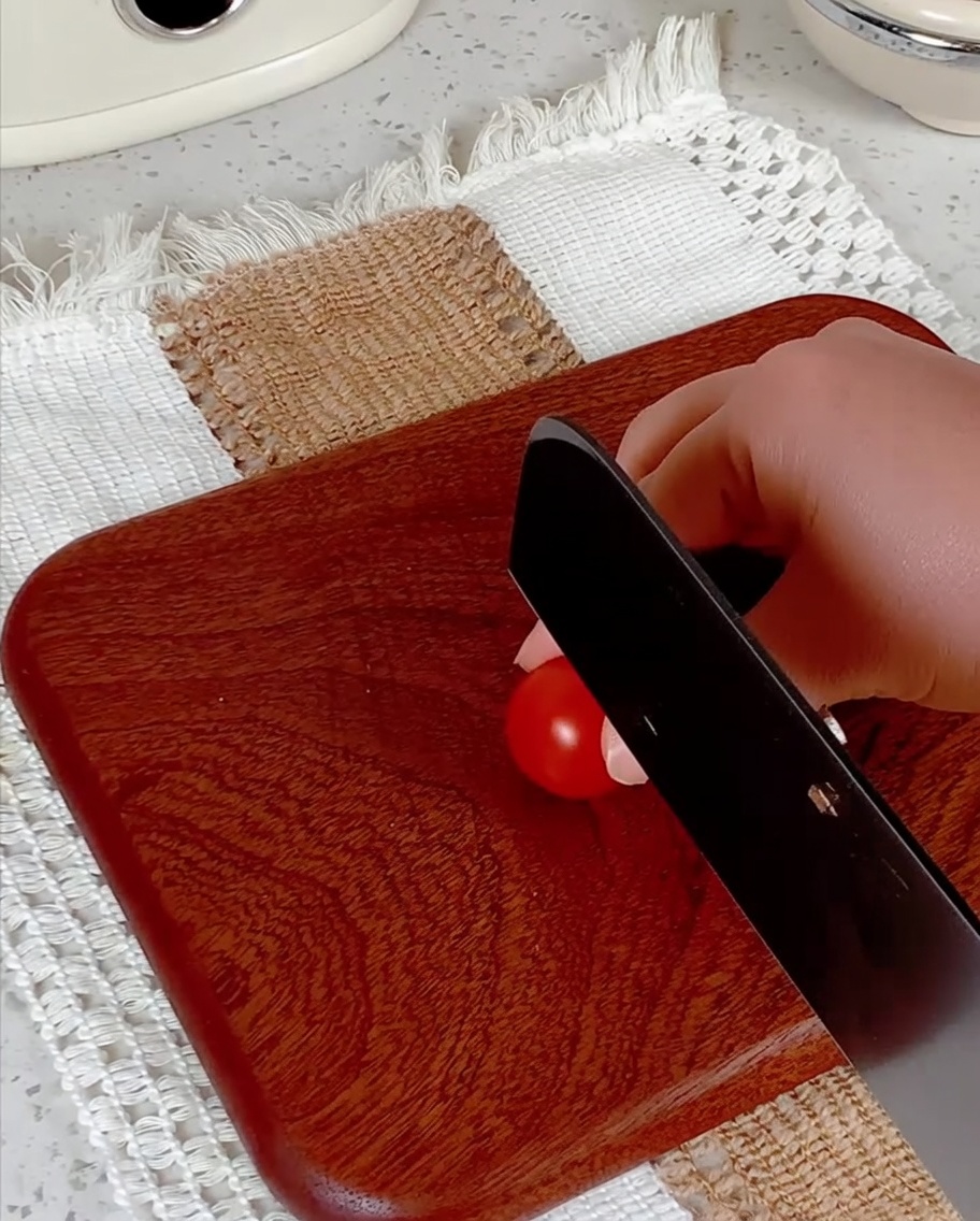 Pomodorini tagliati a metà su un tagliere di legno con un coltello.