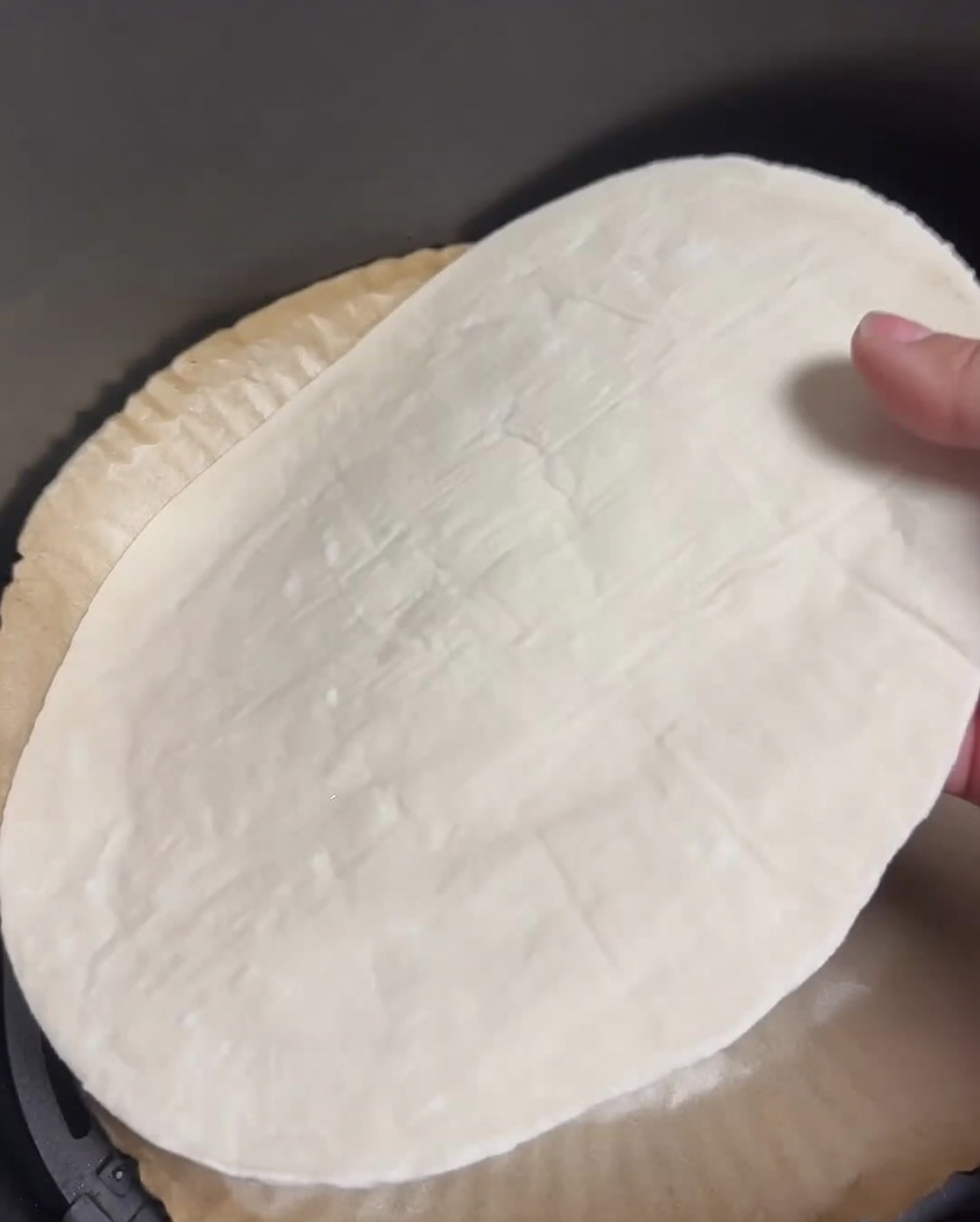 Un pancake alle scalogne crudo poggiato su carta da forno nel cestello della friggitrice ad aria.