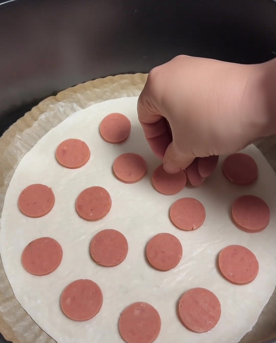 Un pancake alle scalogne guarnito con fettine di salsiccia distribuite uniformemente.