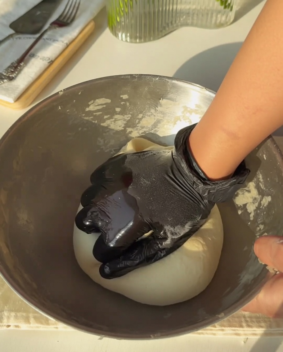 Mano guantata che lavora con fermezza limpasto in una ciotola di metallo finché non diventa liscio e uniforme.