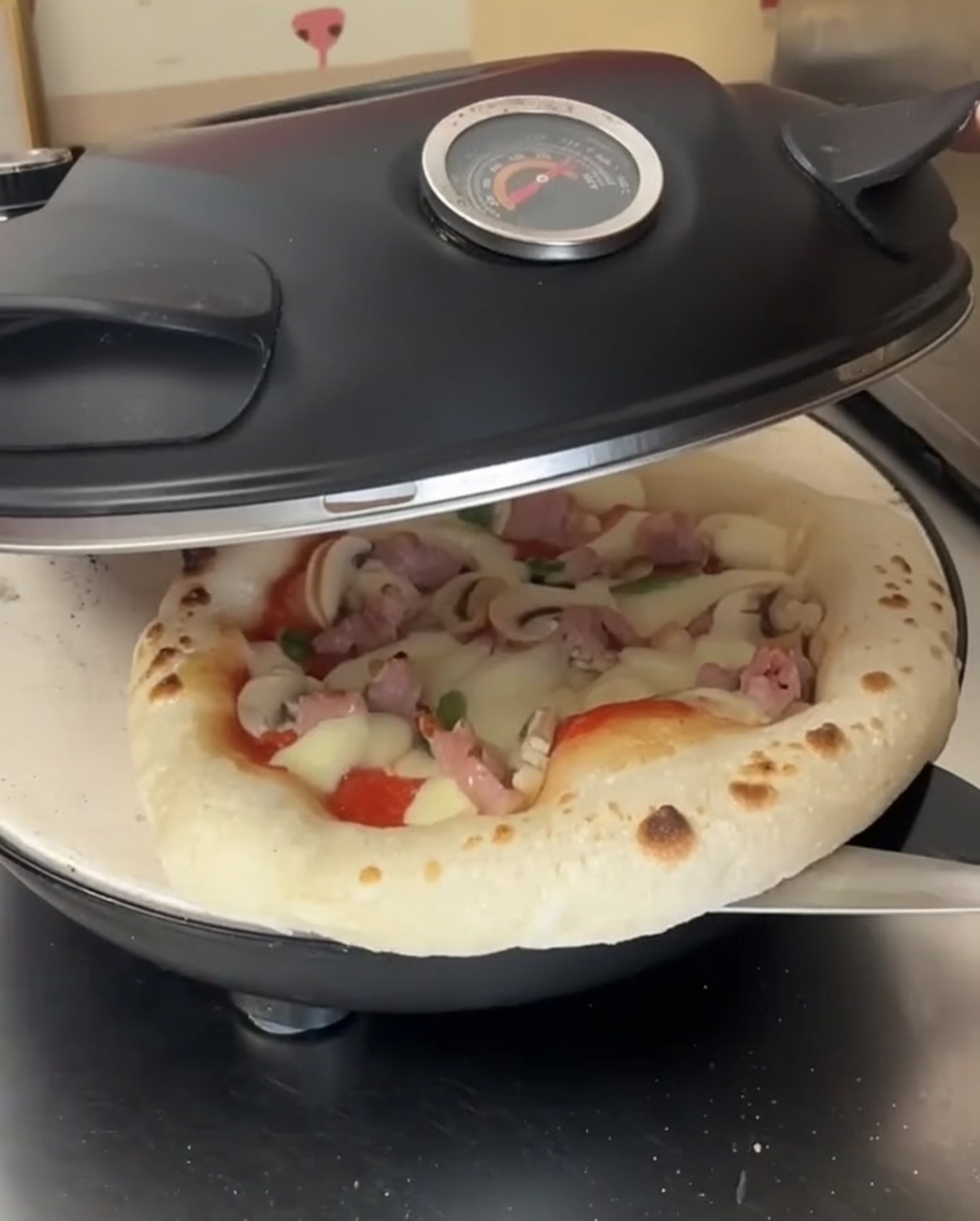 Una pizza a metà cottura con formaggio fuso allinterno del forno, ruotata da una pala in metallo.