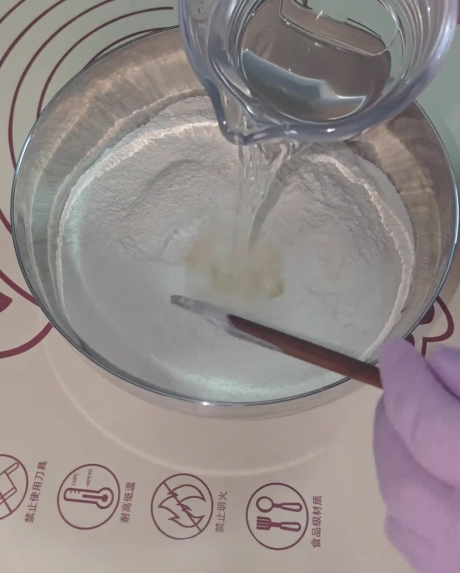 Acqua tiepida versata nel composto di farina, mescolata con bacchette di legno.