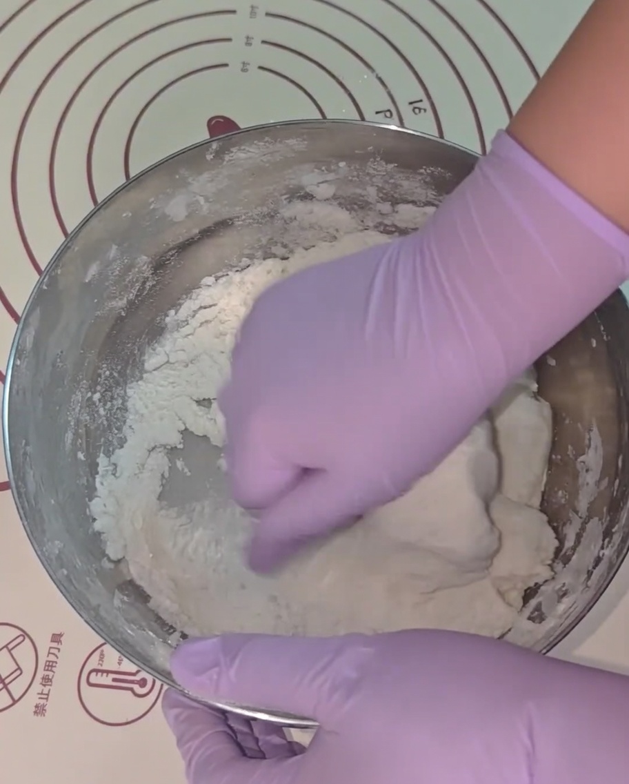 Mani con guanti viola che impastano nella ciotola di metallo.