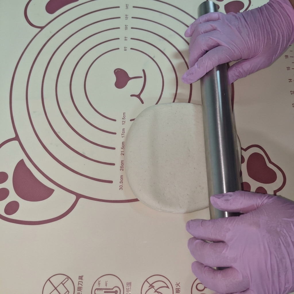 Un pezzo di impasto steso in un disco piatto su un tappetino in silicone con un mattarello.
