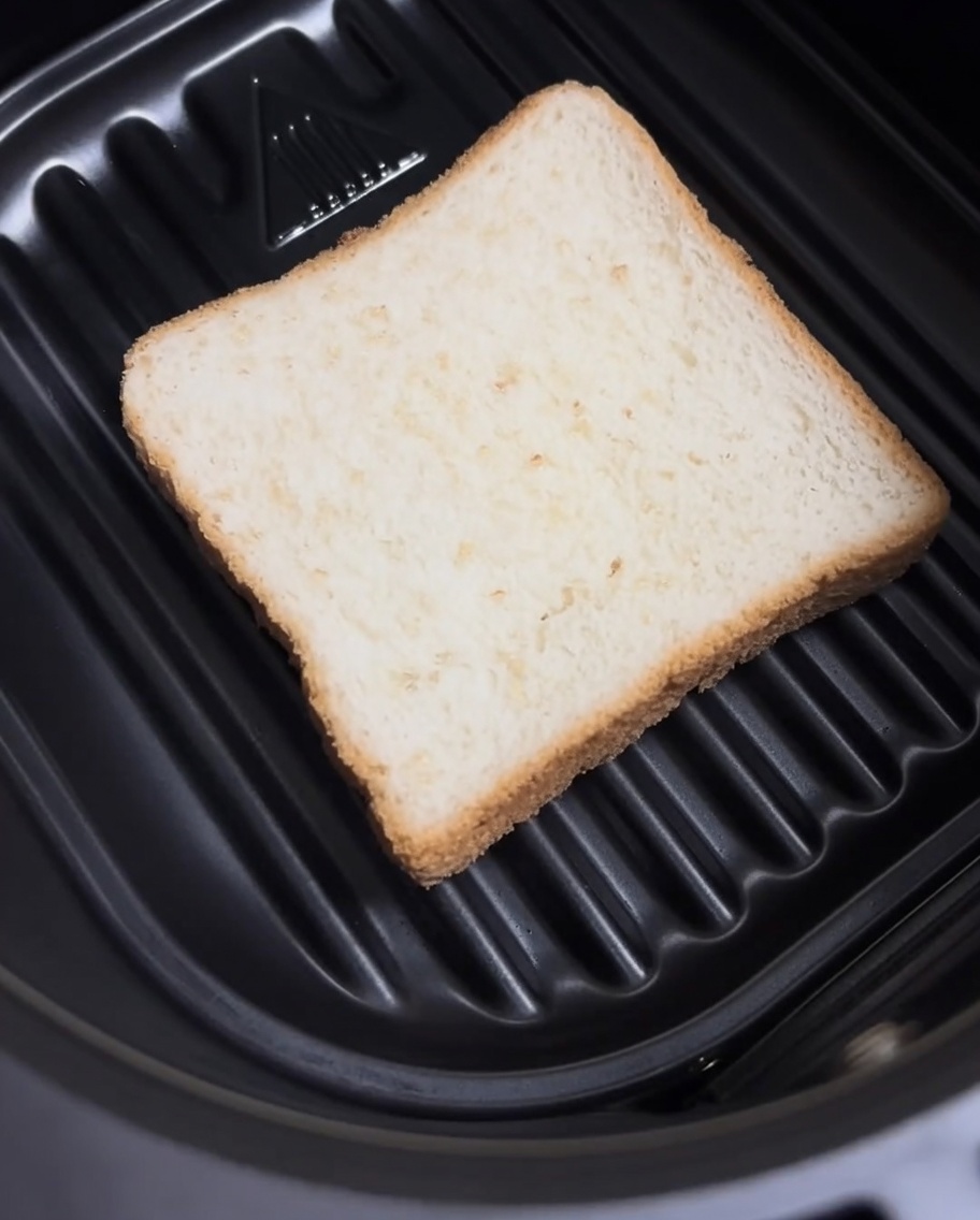 Una fetta di pane bianco appoggiata sul fondo del cestello della friggitrice ad aria.