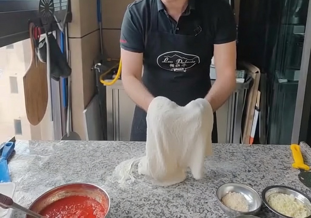 Stendere limpasto per pizza sulle nocche delle mani, tenendolo sollevato verticalmente.