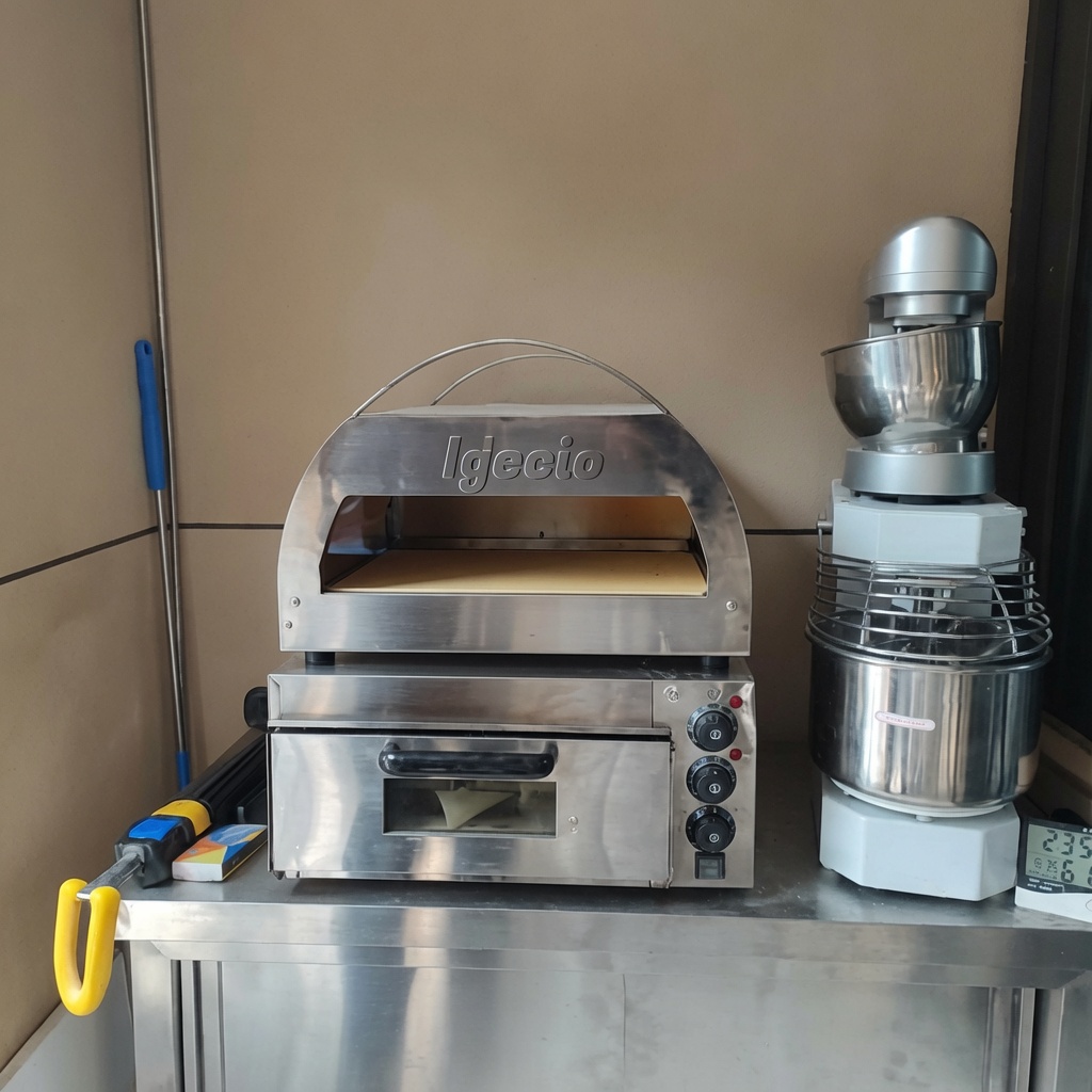 Pizza cruda che viene fatta scivolare in un forno per pizza a gas con fiamme visibili.