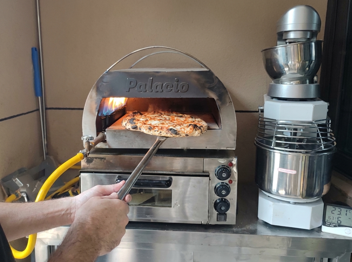 Una pizza perfettamente cotta con il cornicione bruciacchiato estratta dal forno con una pala di metallo.