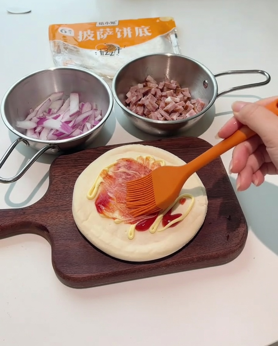 Un pennello in silicone arancione che spalma la salsa rossa e bianca sulla base della pizza.
