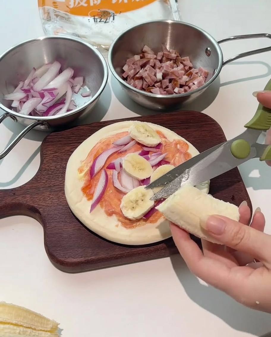 Forbici da cucina che tagliano fette di banana fresca direttamente sopra la pizza.