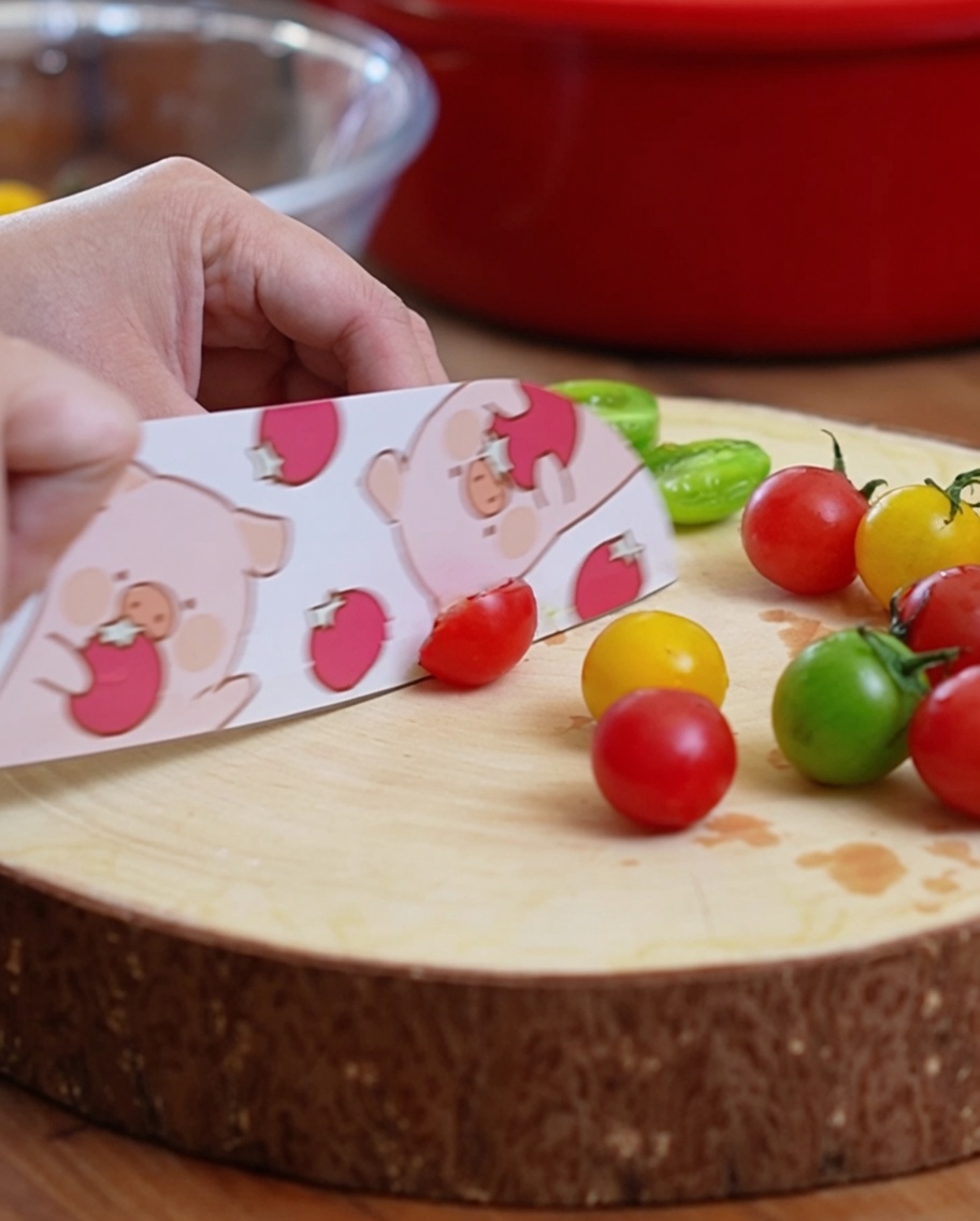 Pomodorini tagliati a metà su un tagliere in legno con un coltello decorato.
