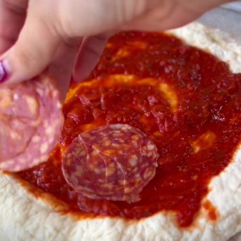 Fette di salame disposte con cura sulla base di pizza condita con il pomodoro.