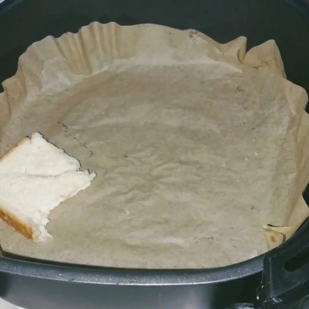 Un primo piano di fette di pane bianco disposte ordinatamente nel cestello della friggitrice ad aria foderato con carta forno.