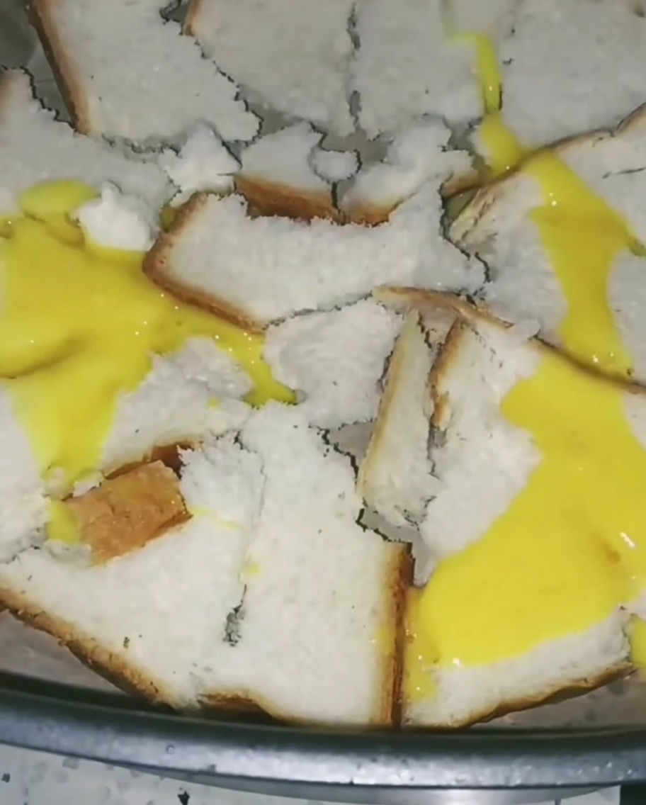 Uova sbattute versate sopra il pane nella friggitrice ad aria, creando un sottile strato giallo sulle fette.