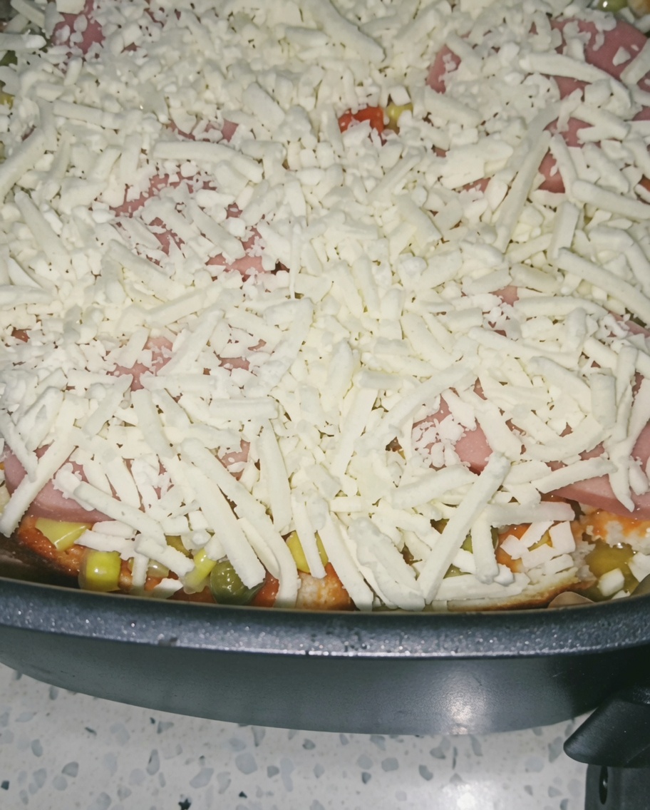 Un primo piano di un generoso strato di mozzarella grattugiata che copre il prosciutto e le verdure nella friggitrice ad aria.