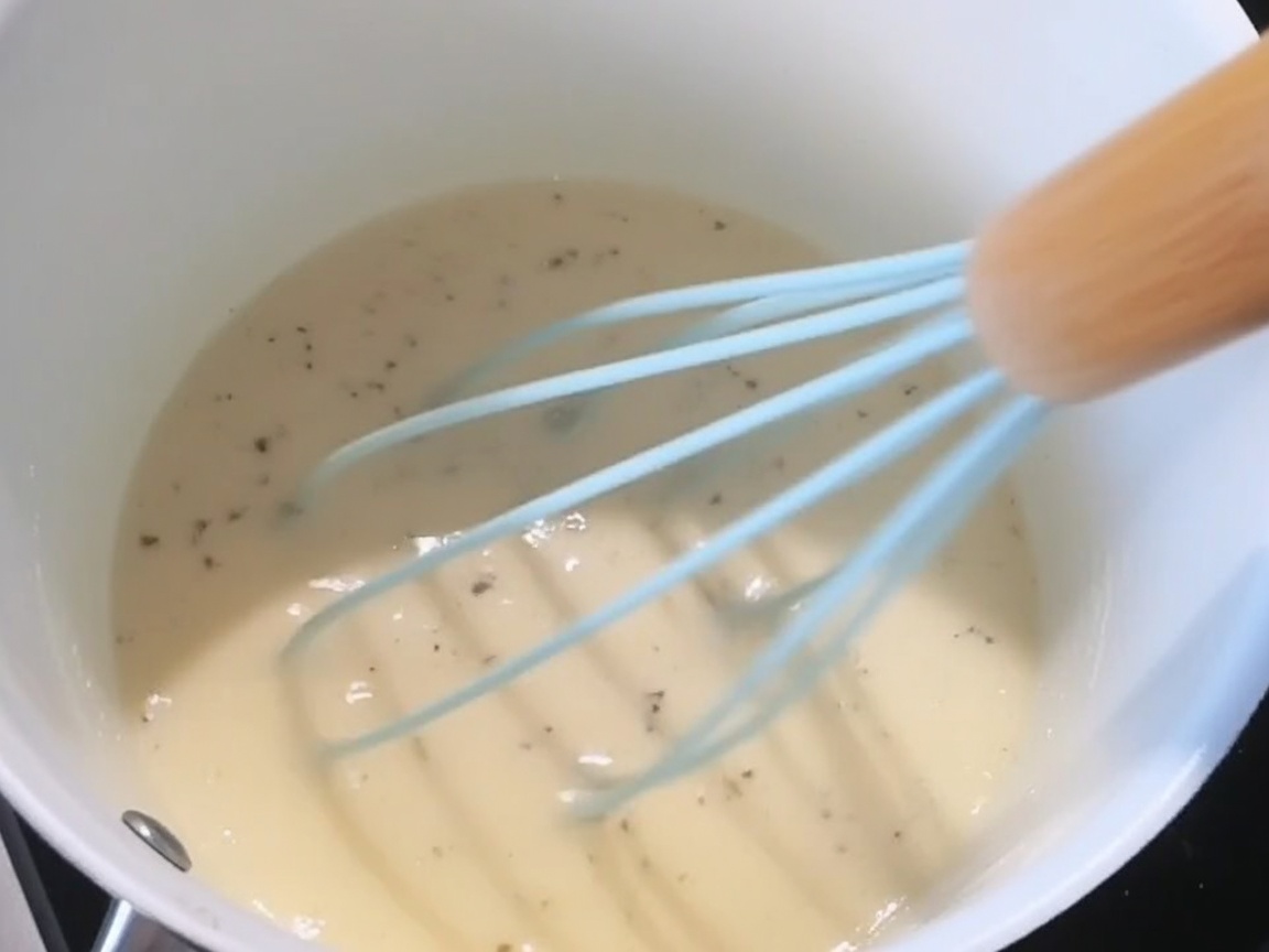 Sale, pepe nero e formaggio grattugiato vengono aggiunti alla salsa bianca cremosa.