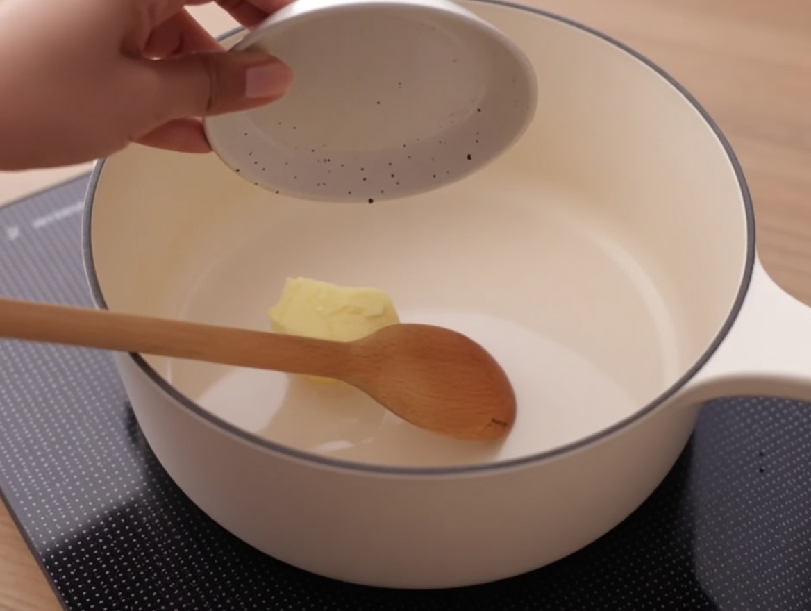 Un panetto di burro che si scioglie in un pentolino bianco su un fornello.