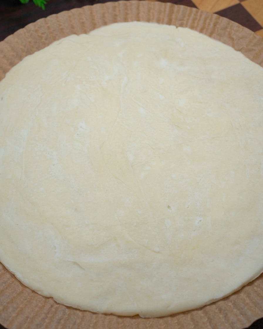 Primo piano delle mani che modellano i bordi di un pancake crudo su carta forno per formare il bordo di una pizza.