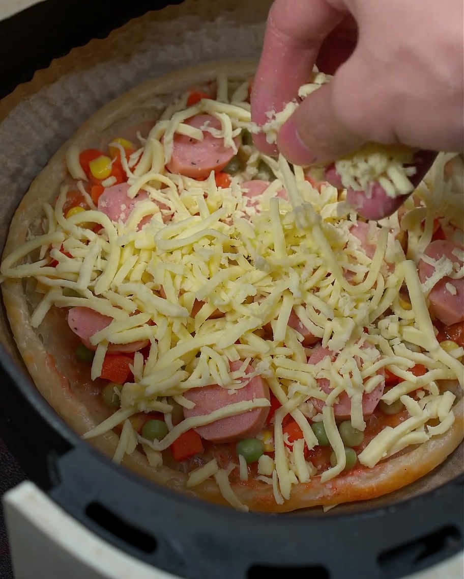 Primo piano della mozzarella grattugiata che viene cosparsa sopra gli ingredienti della pizza.
