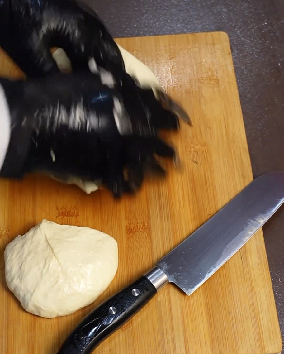 Quattro porzioni uguali di impasto per pizza su un tagliere in legno accanto a un coltello.