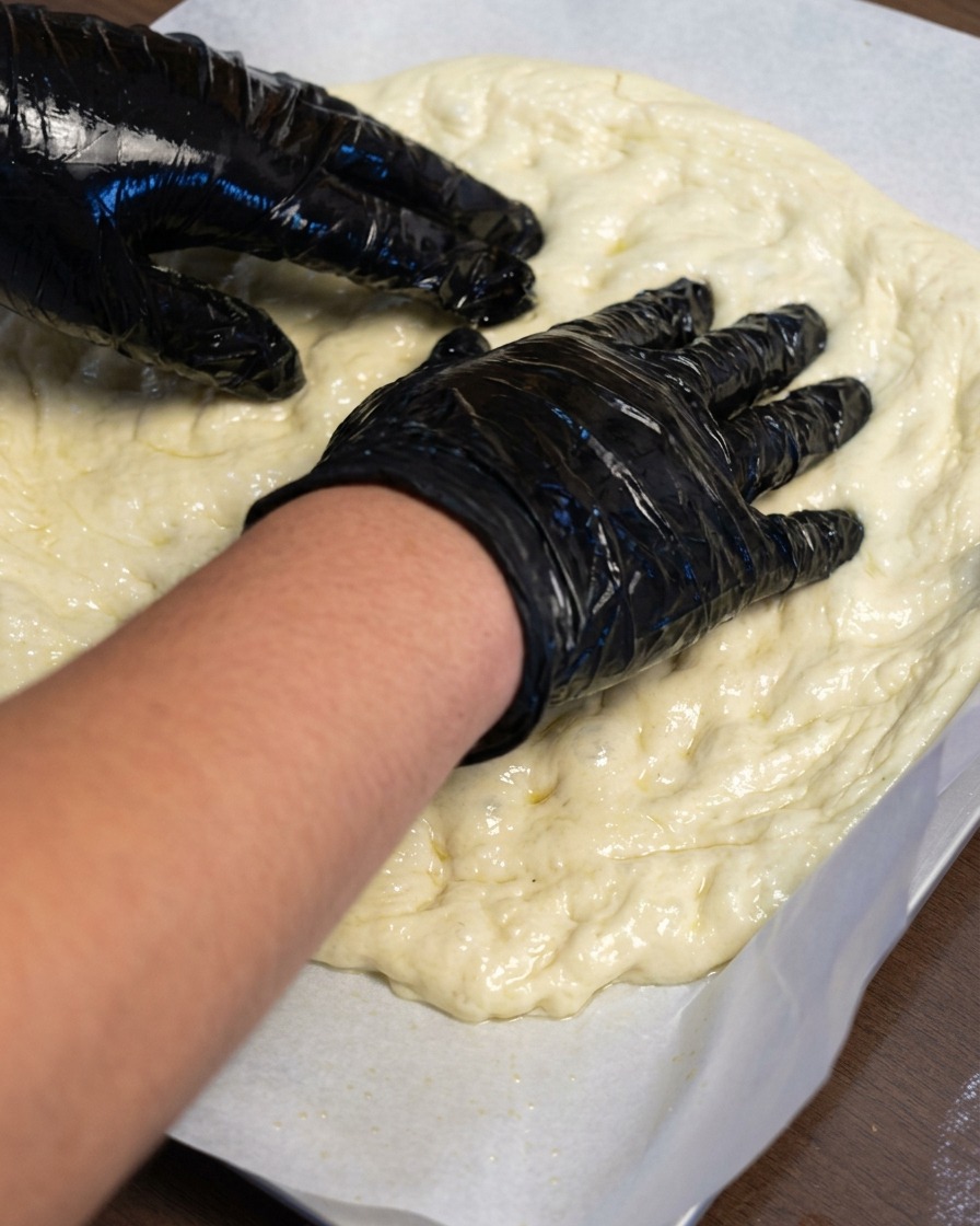Mani che stendono limpasto della pizza su un foglio di carta forno.