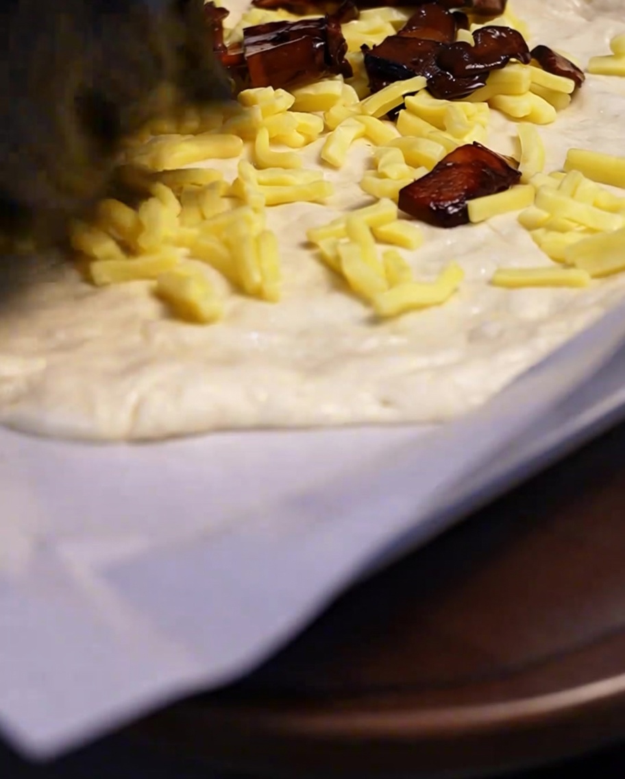 Funghi cotti e conditi distribuiti con un cucchiaio sopra uno strato di mozzarella su una base di pizza.