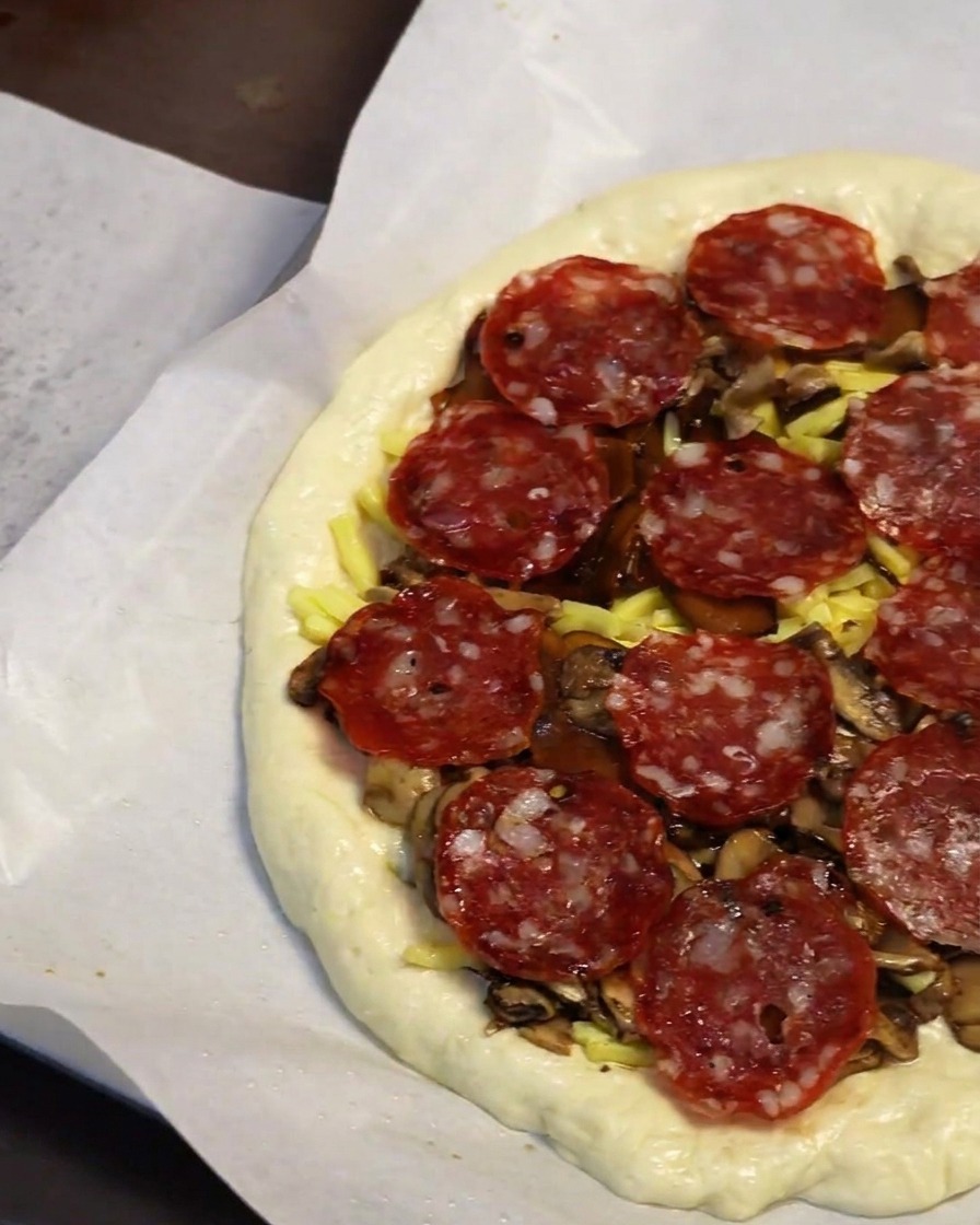 Primo piano di una mano che posiziona fette di salame piccante sulla pizza.