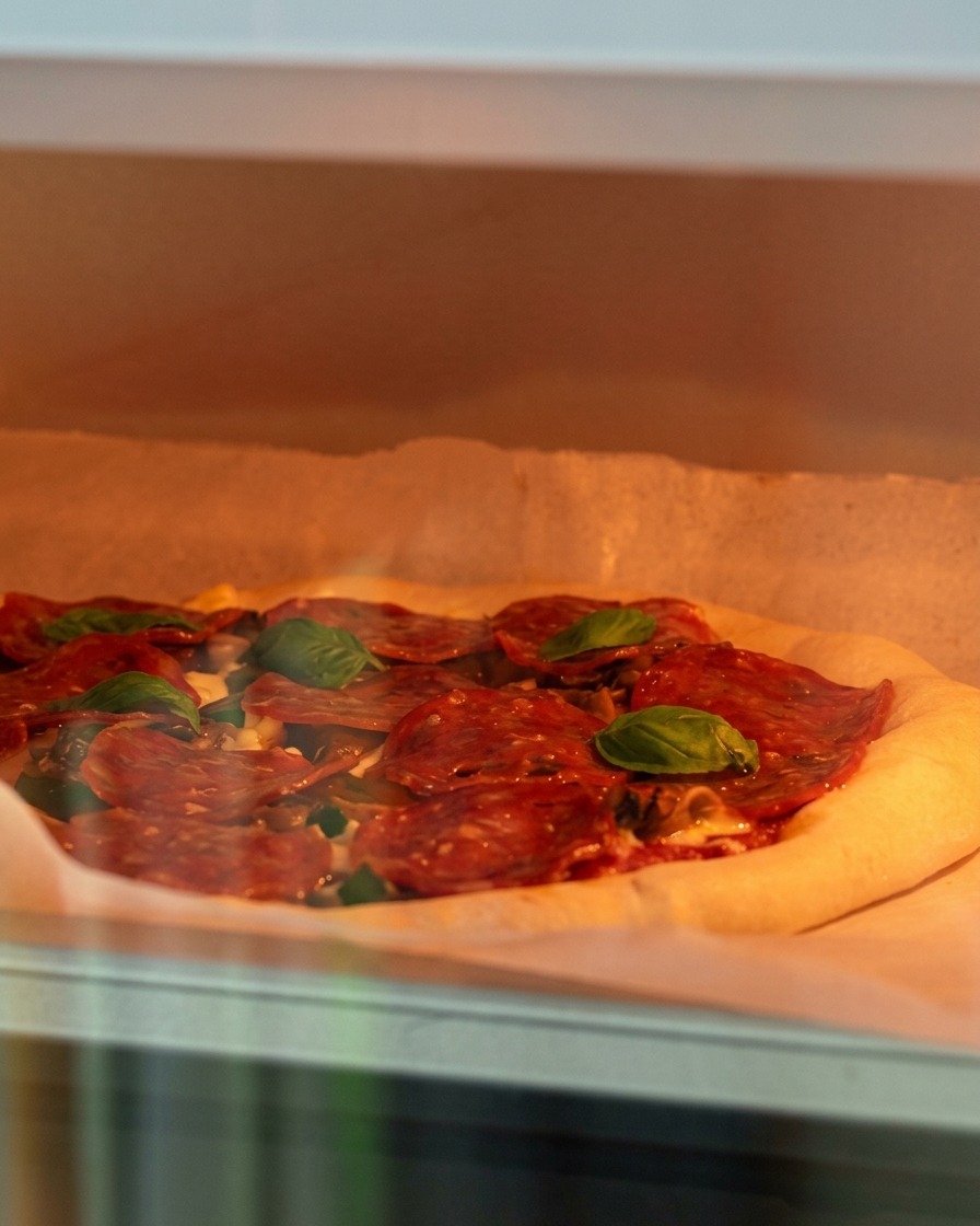 Una pizza cruda guarnita con formaggio, funghi e salame piccante inserita in un forno caldo.