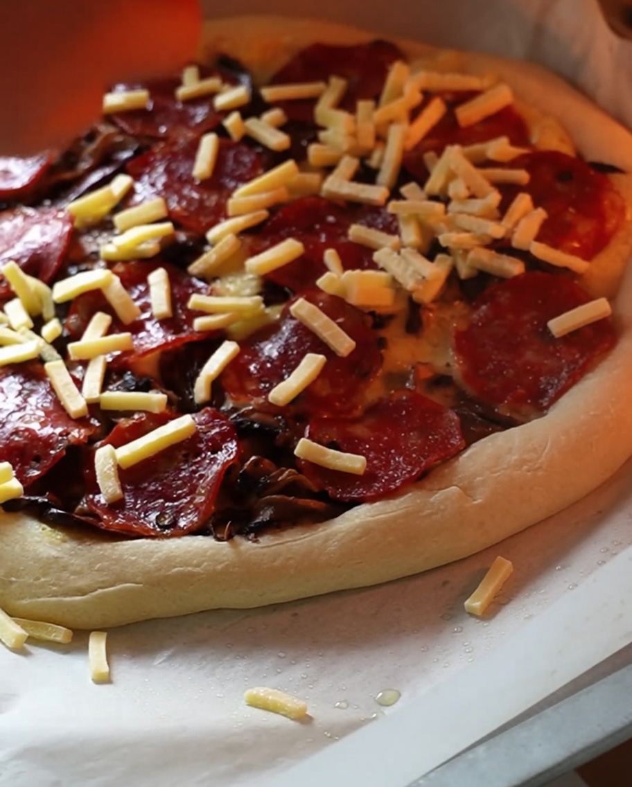 Una pizza parzialmente cotta in forno con una generosa manciata finale di formaggio grattugiato.
