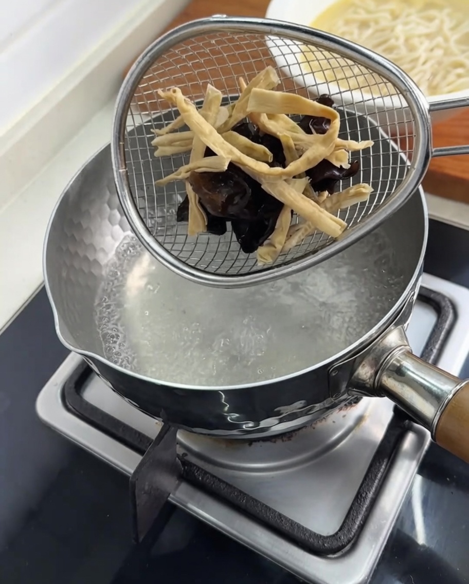 Funghi orecchio di Giuda e germogli di bambù sbollentati in un colino allinterno di una pentola di acqua bollente.
