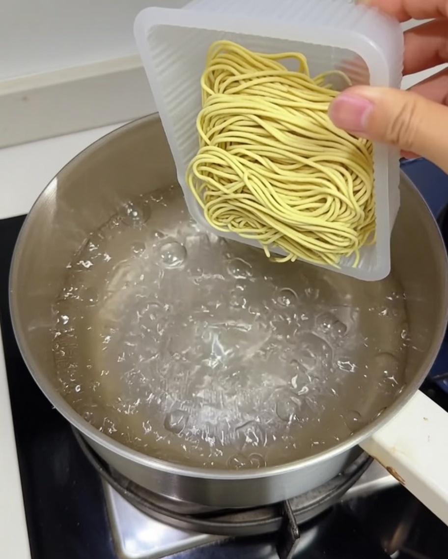 Un panetto di noodles ramen freschi gialli immersi in una pentola di acqua bollente.