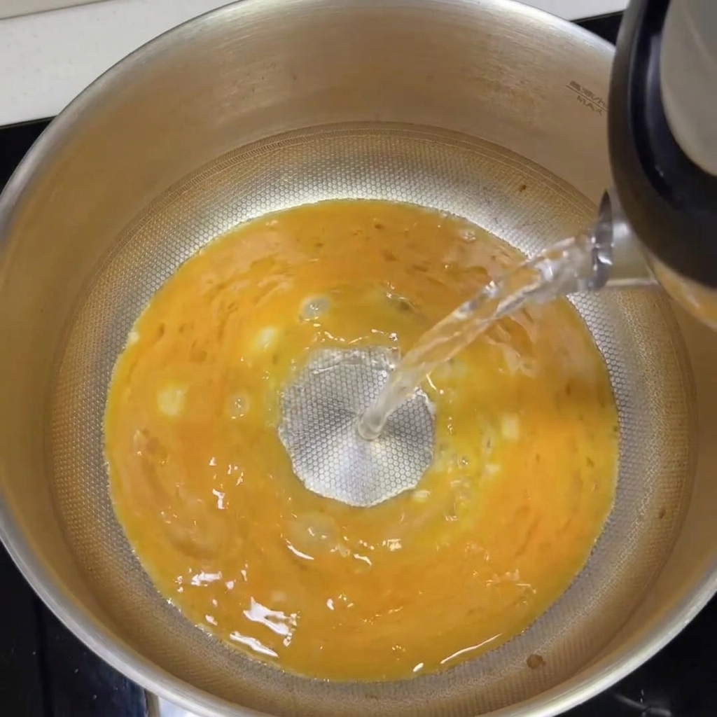 Acqua bollente versata nella pentola con la base tonkotsu, trasformandosi in un brodo bianco cremoso.