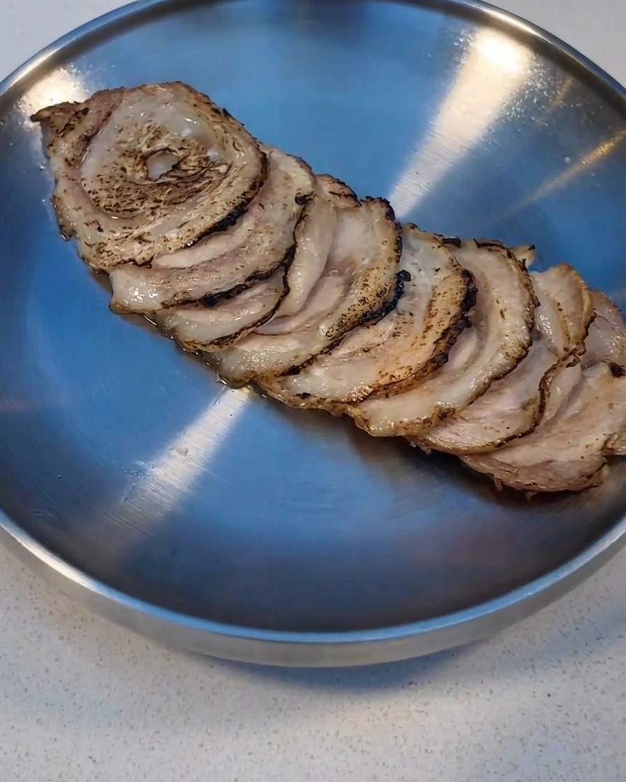 Fette di Char Siu scottate con un cannello da cucina su un vassoio di metallo.