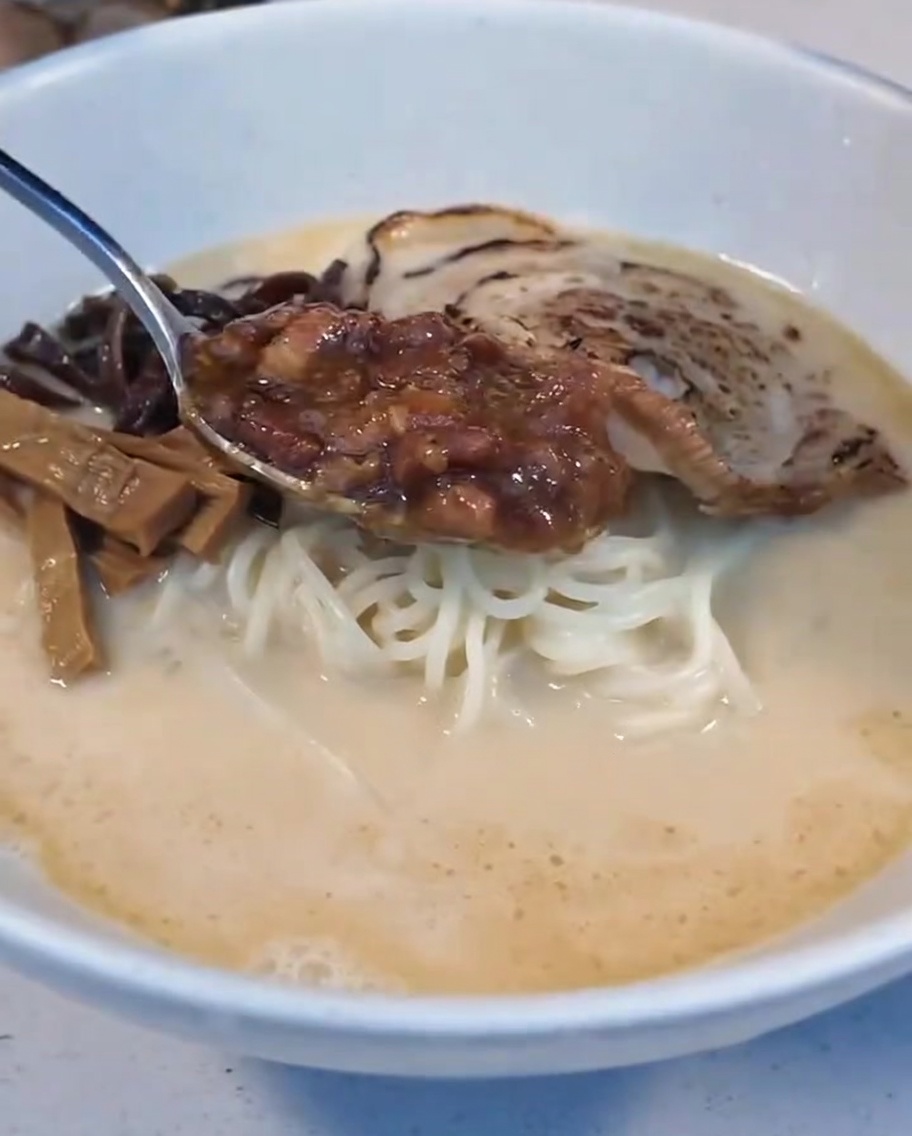 Un cucchiaio di salsa di carne brasata aggiunto nella ciotola del ramen accanto a mezzo uovo barzotto.