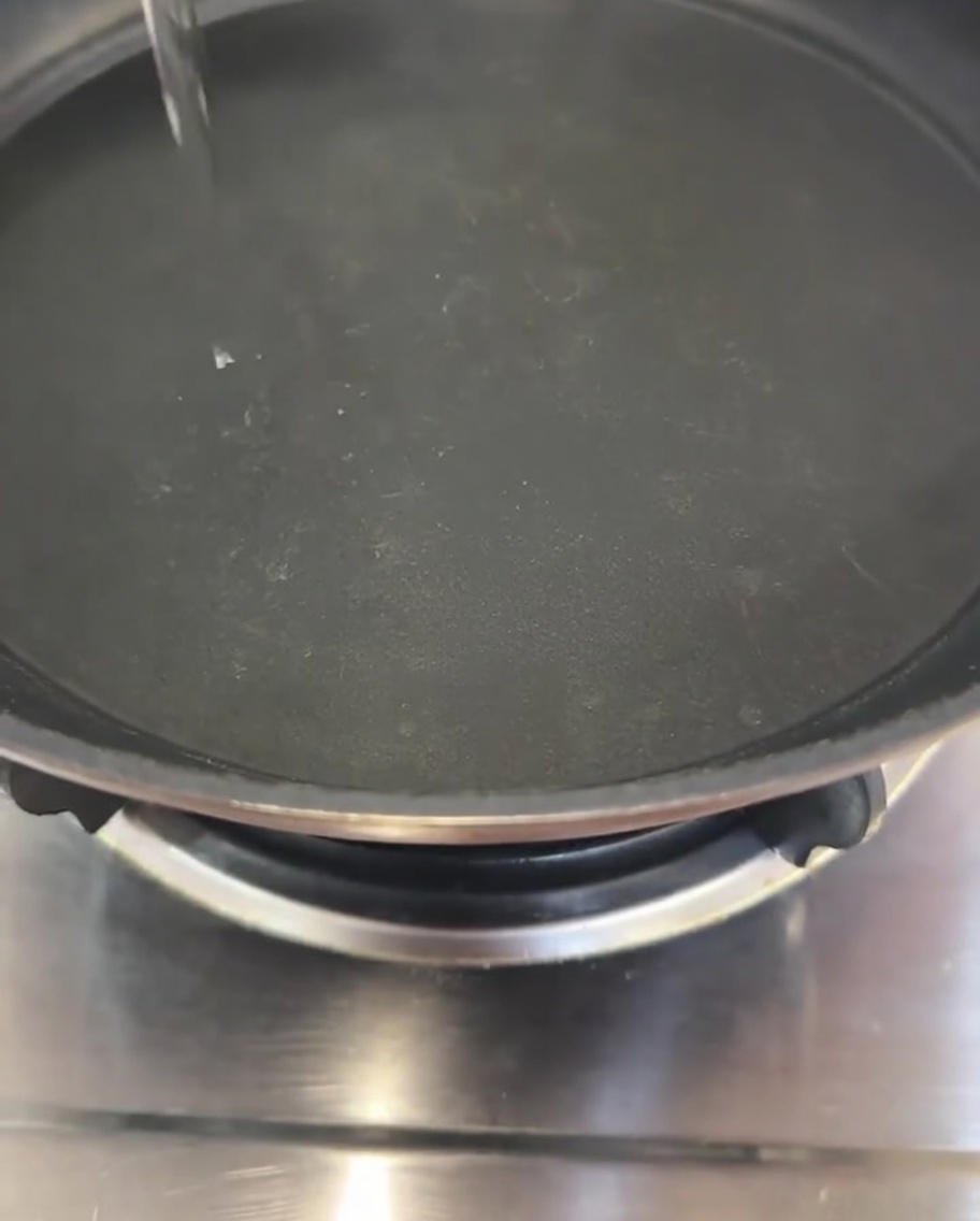 Un filo sottile di olio versato al centro di una padella nera.