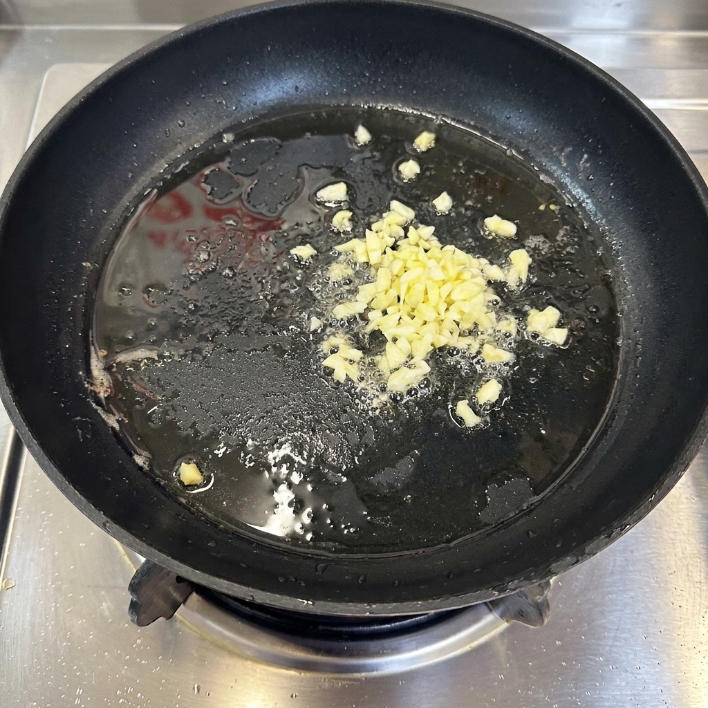 Aglio finemente tritato che sfrigola in un sottile strato di olio caldo allinterno di una padella nera.