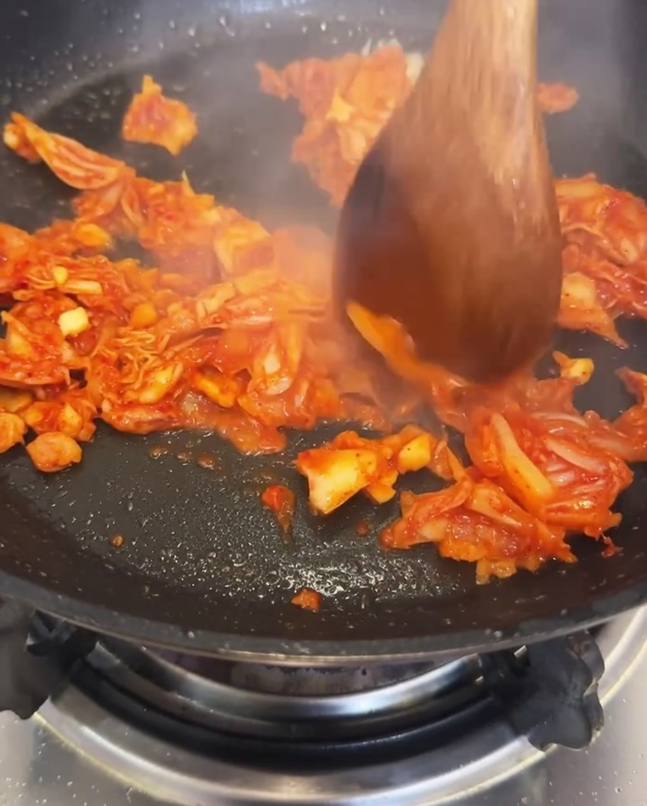 Acqua versata nella padella contenente kimchi e aglio saltati.