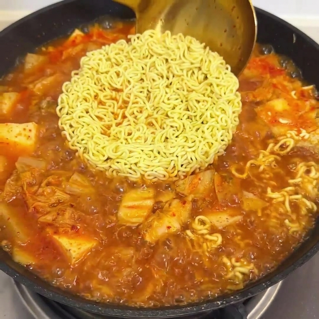 Salsa rossa versata in una padella con noodle ramen in ebollizione e brodo di kimchi.