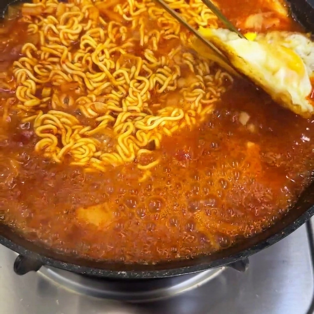 Uova fritte aggiunte a una padella con noodle ramen piccanti in ebollizione.