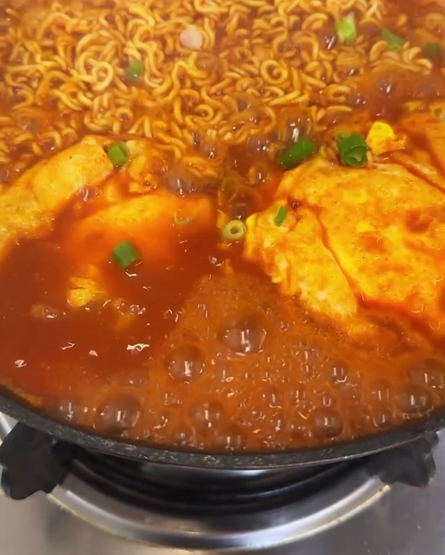 Una vista ravvicinata di una pentola di ramen al kimchi guarnito con cipollotto fresco e fette di peperoncino rosso vivo, con il brodo che bolle intorno.