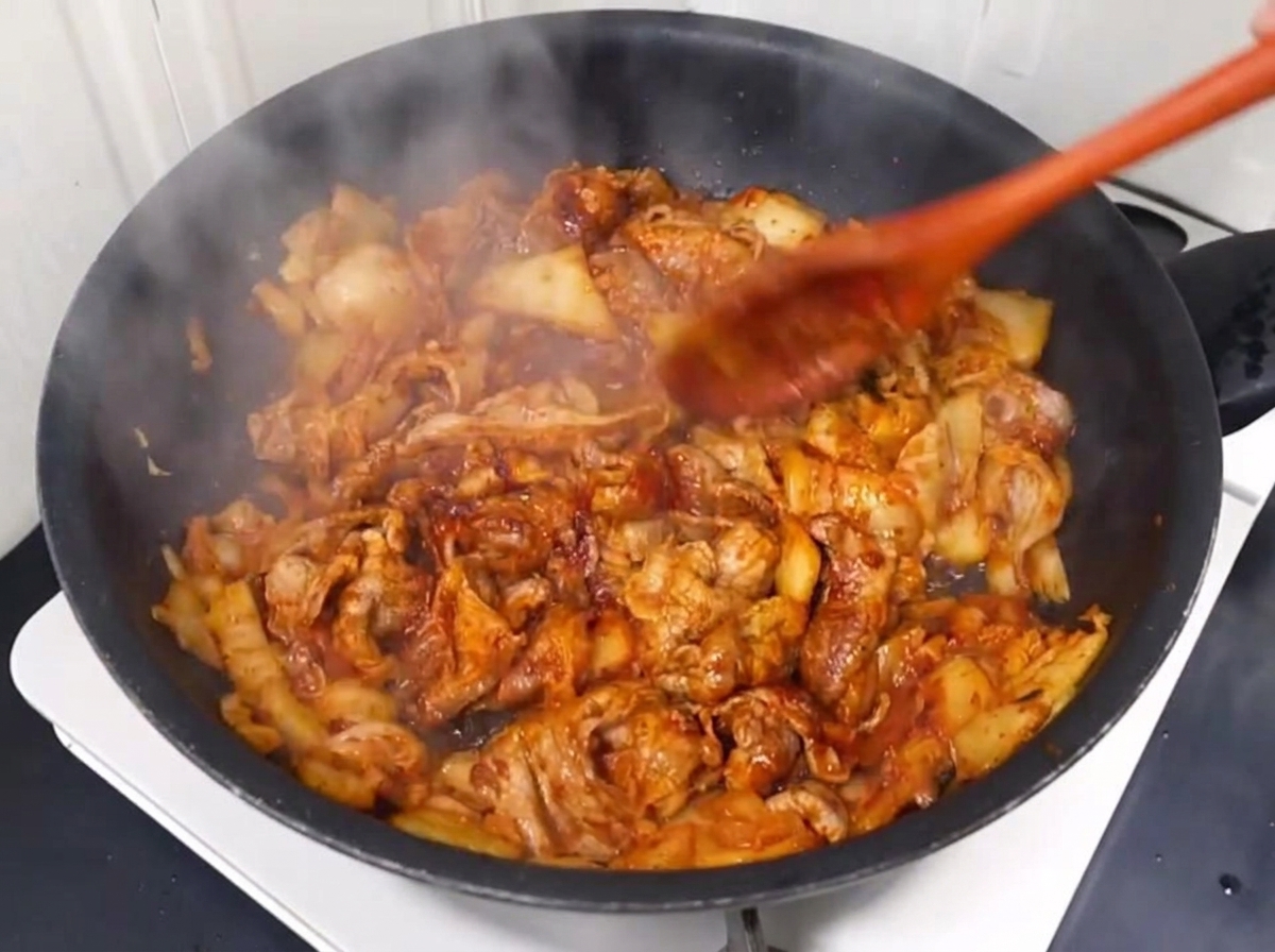 Acqua versata nella padella sopra il maiale e il kimchi.