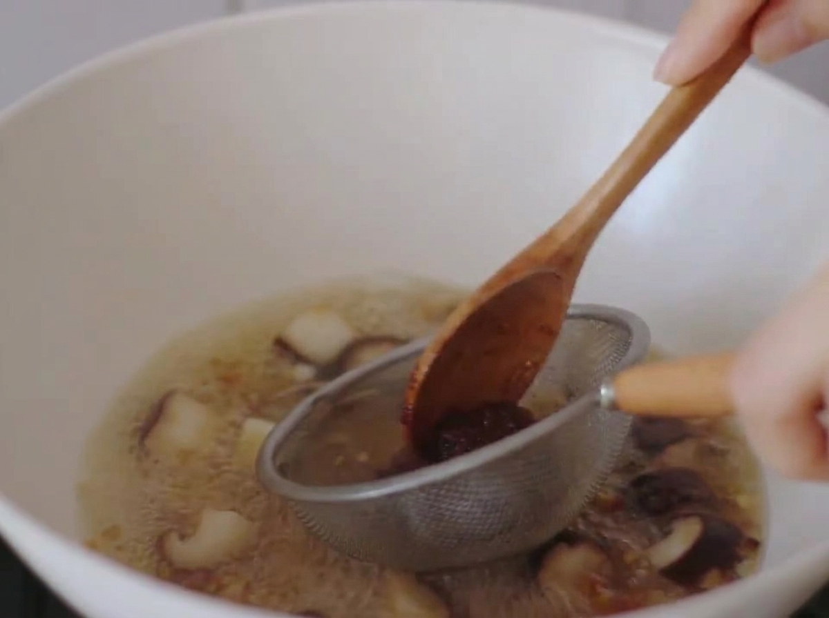 La pasta di miso viene sciolta nel brodo bollente utilizzando un piccolo colino di metallo e un cucchiaio di legno.