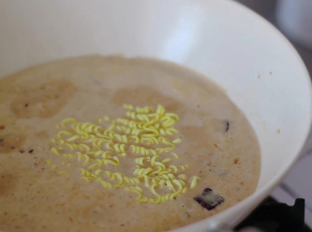 Noodles istantanei e fettine di narutomaki bollono in un brodo cremoso.