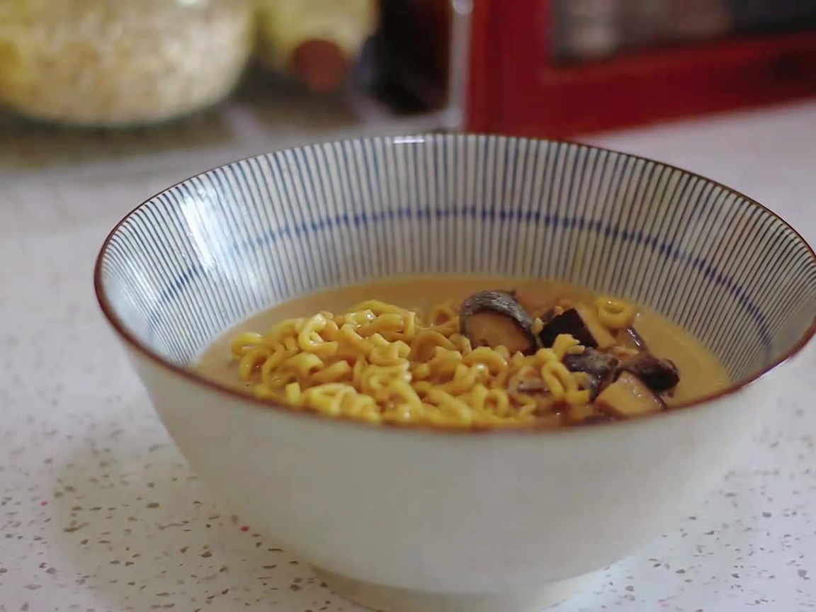 I noodles e il brodo cremoso vengono versati in una ciotola a righe con un mestolo.