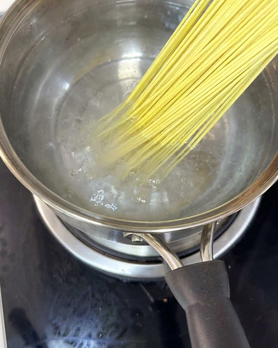Noodles immersi in una pentola di acqua bollente, mescolati con le bacchette.