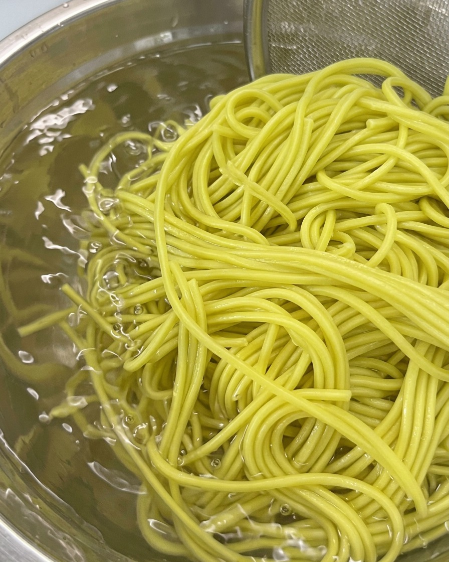 Uno scolapasta con noodles bolliti immerso in una ciotola di acqua fredda per il risciacquo.