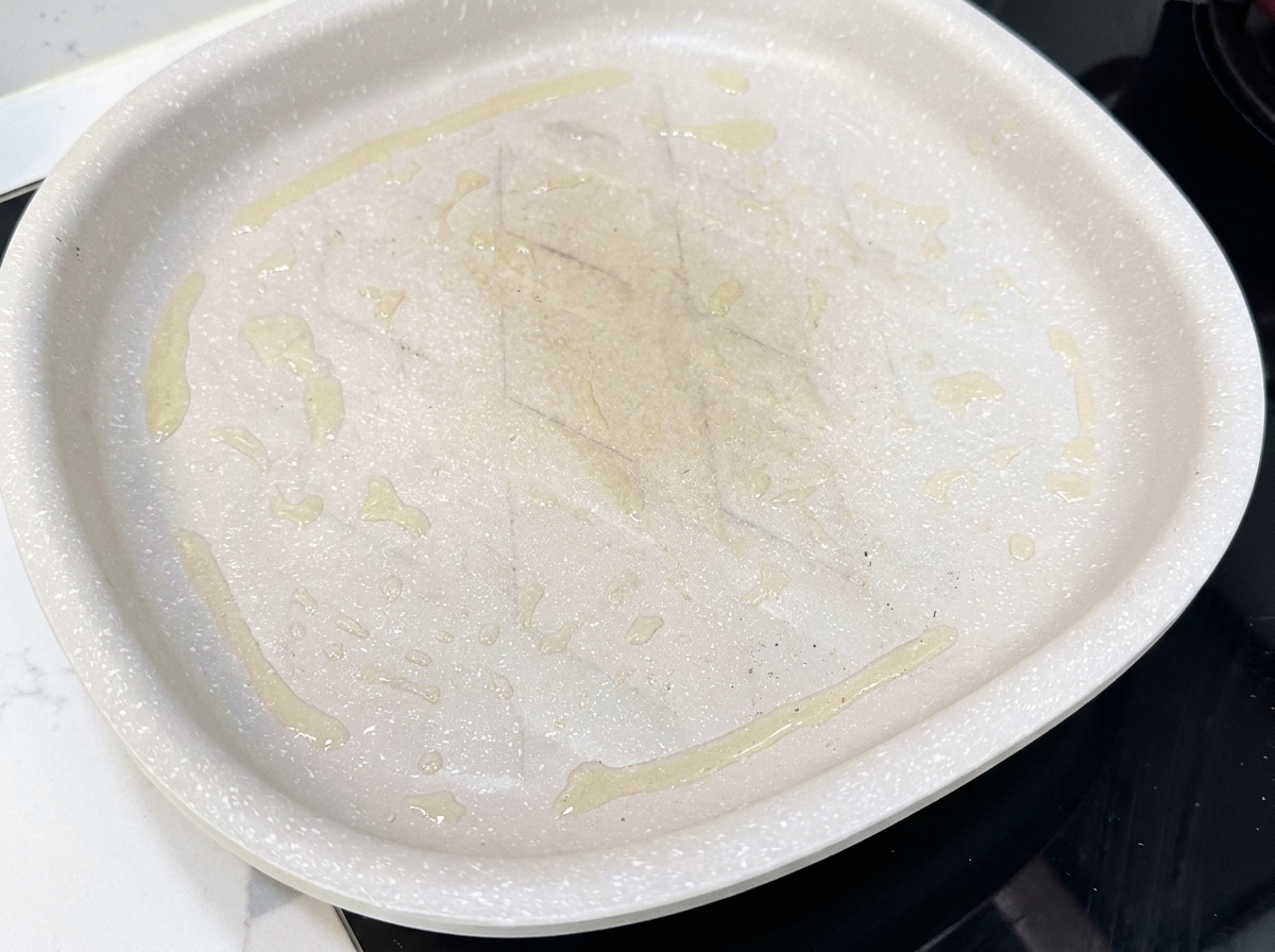 Fette di pancetta adagiate in una padella antiaderente calda, che iniziano a cuocere.