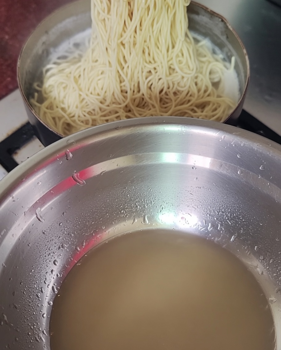 Noodle cotti sollevati da una pentola con le bacchette.