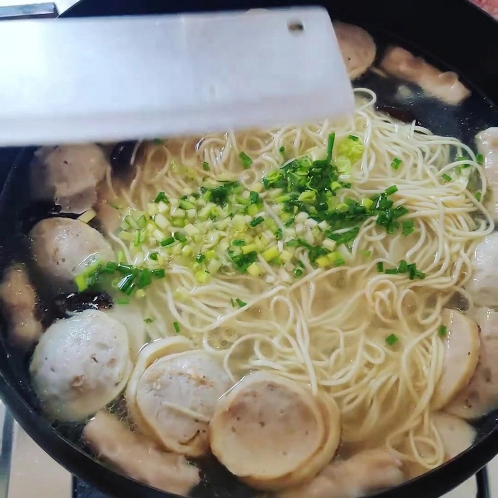 Vista dallalto di una pentola contenente noodle, polpette e altri ingredienti guarniti con cipollotti tritati.