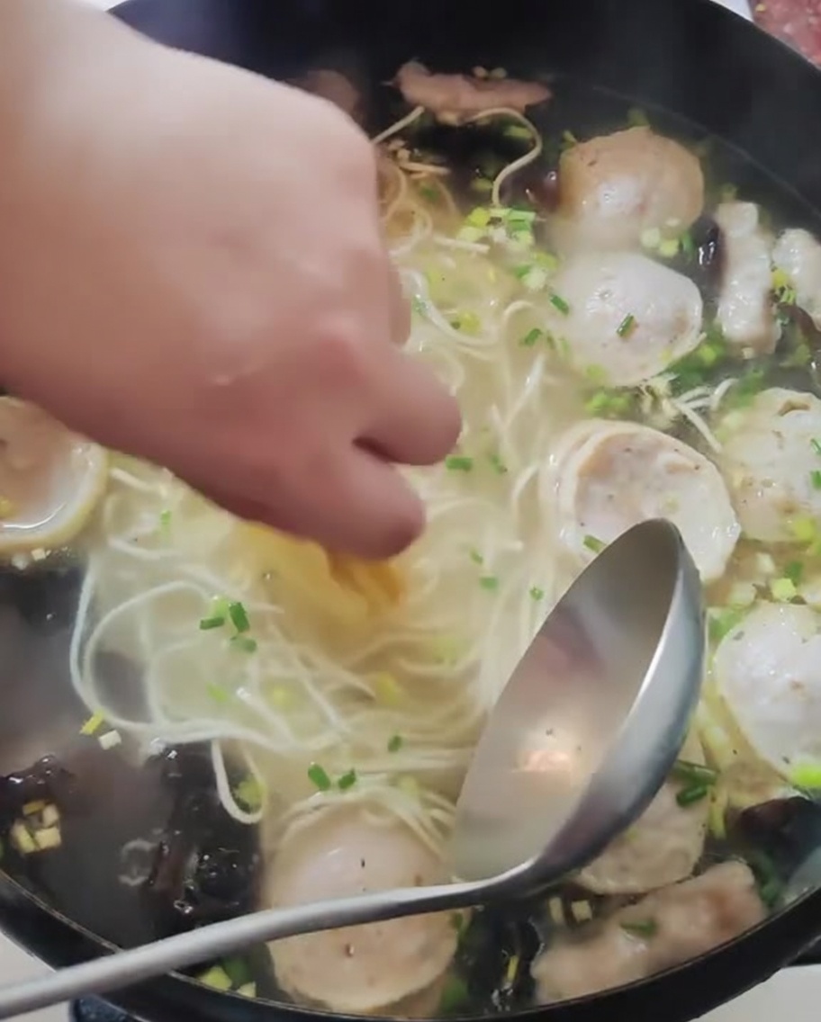 Una mano posiziona fette sottili di limone giallo in una pentola di noodle cotti e brodo.
